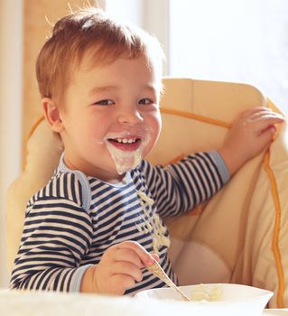 Two year old boy smiles to the camera eating porridge.