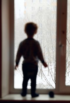 Boy stands on the windowsill and looking through the window.