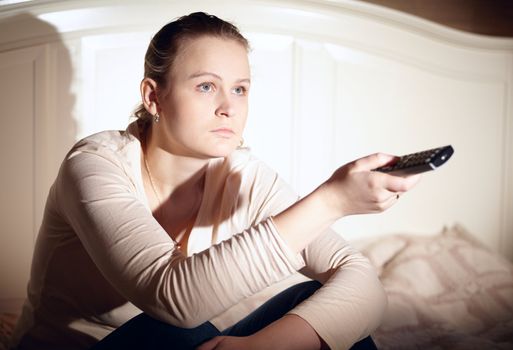 Young woman is watching tv with remote control.