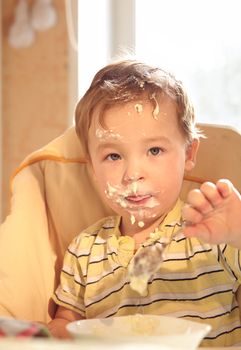 Portrait of two year old boy in the baby chair eating porridge in the morning.