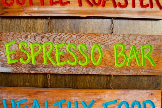 A handmade wood sign on a wood background is carved out and painted showing the words espresso bar in green letters.