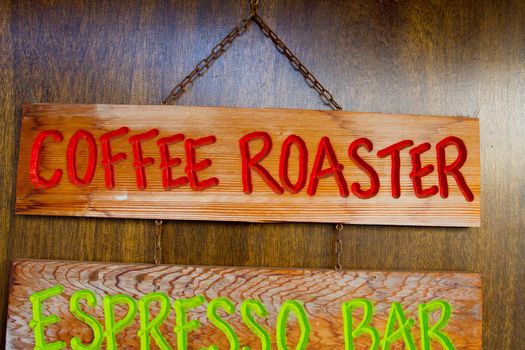 A handmade wood sign on a wood background is carved out and painted showing the words coffee roaster in red letters.