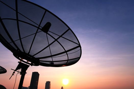 black antenna communication satellite dish over sunset sky in cityscape