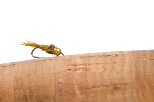 Isolated in a studio with a white background a hares ear nymph in natural colors is photographed closeup against the cork handle of a fly fishing rod.