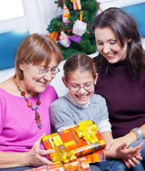 Cute girl and her mother and grandmother watching Christmas gifts