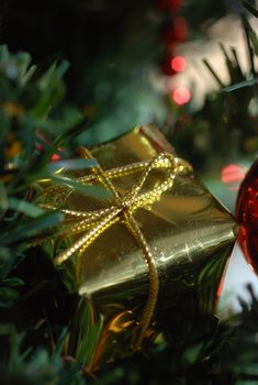 Close up of small golden Christmas decoration in the shape of a parcel. against dark green of Christmas tree.