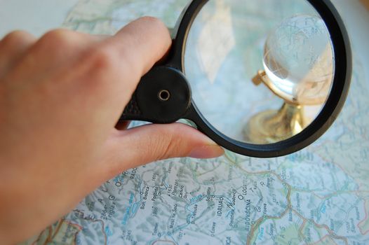 Woman's hand holding magnifying glass over map and globe