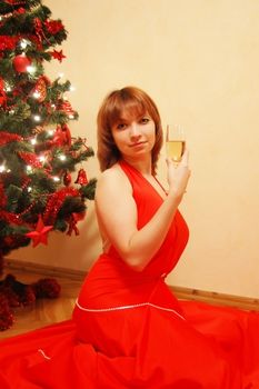 Beautiful girl in red dress near Xsmass tree with glass