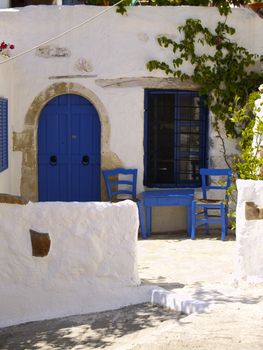 table and two chairs in front of an old greek house