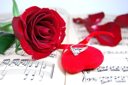 red rose and petals on music sheet with fabric heart