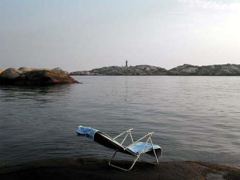 Lonely chair in Norwegian coastline.
Svenner lighthouse in background. 