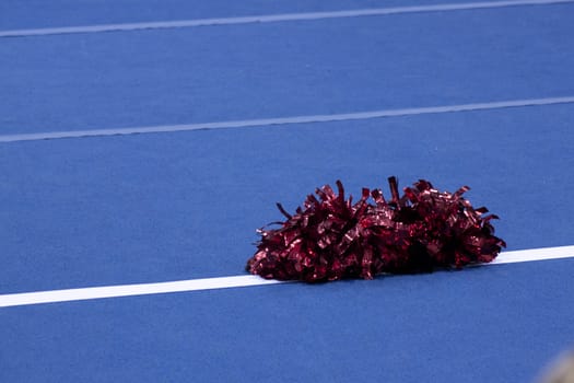 Cheerleading compitition pom poms on a blue mat with lines.