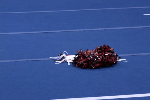 Cheerleading compitition pom poms on a blue mat with lines.