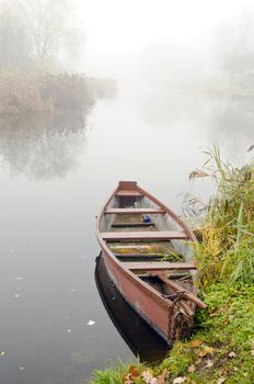 Wooden rowing boat stands on coast of river sunken in dense fog.