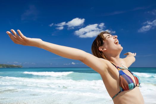 Beautiful young woman with arms open in a tropical beach enjoying the summer 