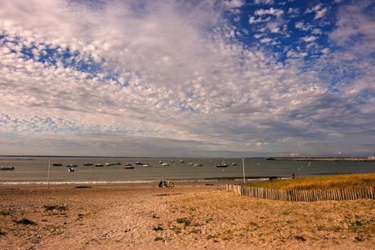 View over sandy beach of small boats anchored off shore against a cloudy sky