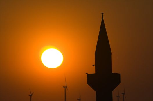 Minaret and wind turbines against a setting sun 