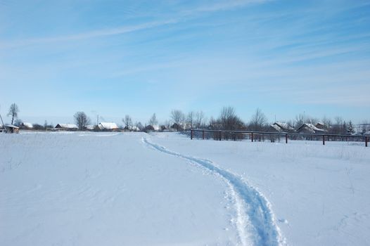 Narrow winter path in field to a small village, sunny winter day