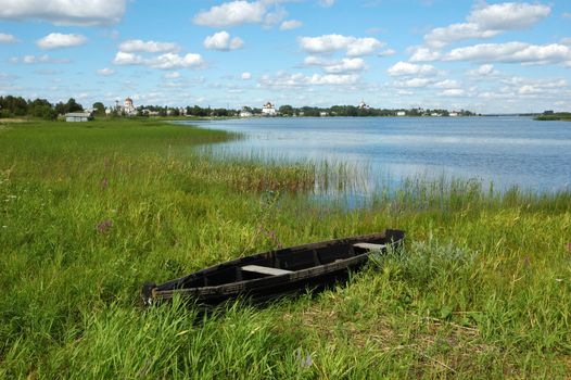 View of ancient russian town Kargopol, destroyed wooden boat on river bank, clouds in sky