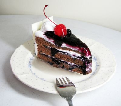 a slide of black forest cake with cherry on top and white chocolate