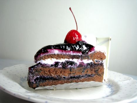 a slide of black forest cake with cherry on top and white chocolate