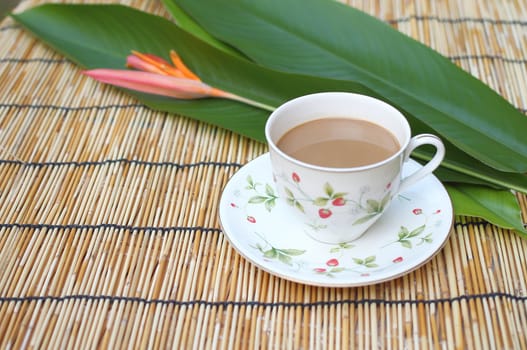 Cup of coffee with one heliconia flower, put on the table cloth made from wooden.