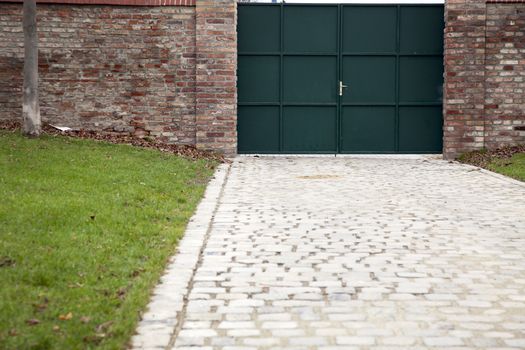 Cobble driveway leading to green gate and brick wall.