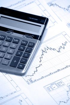 Calculator laying on printed stockcharts with bullish trend. Cold photofilter.