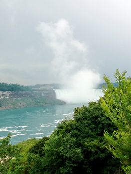 Niagara fall behind vegetation and with coud of water, Ontario, Canada