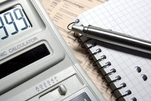 Calculator with numbers on display, pen and notebook laying on newspaper.