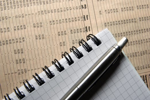 Pen and notebook laying on newspaper with financial data.