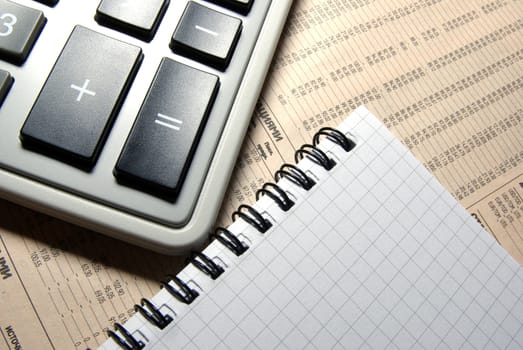 Calculator and notebook laying on financial newspaper.