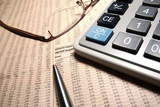 Glasses, professional calculator and steel pen on newspaper.