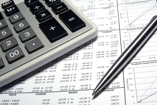 Calculator, steel pen and financial data with graphs.