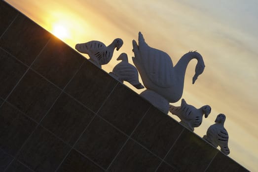 Silhouette of swan's sculptures with sunset on background.