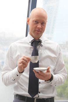 The businessman drinks coffee at office from a small white cup