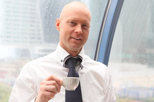 The businessman drinks coffee at office from a small white cup