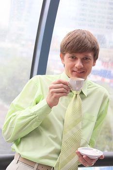 The businessman drinks coffee at office from a small white cup