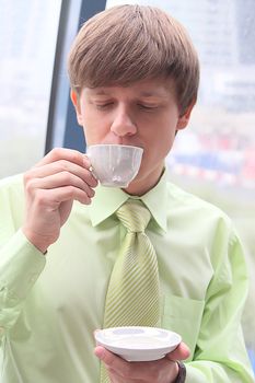 The businessman drinks coffee at office from a small white cup