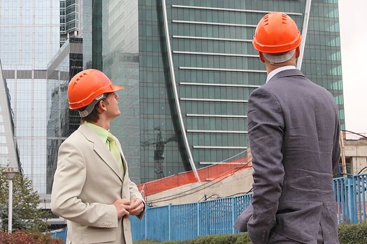 Two businessmen in business suits and helmets on building