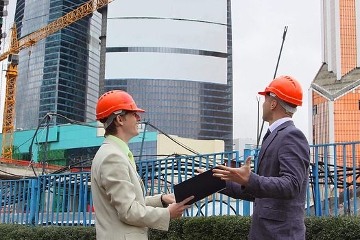 Two businessmen in business suits and helmets on building