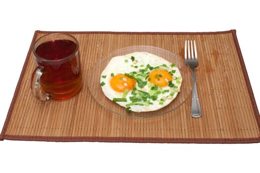 Fried eggs with green onions and a cup of tea on a bamboo mat.