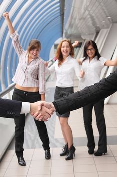 Hand shake of two businessmen against happy colleagues
