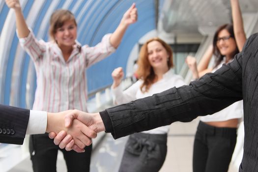 Hand shake of two businessmen against happy colleagues