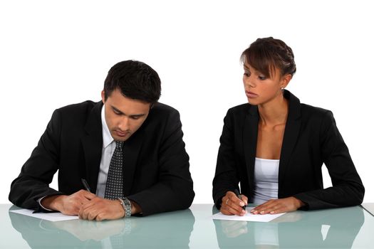 Two businesspeople writing at a desk