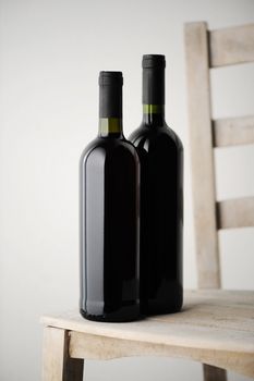 two bottles of red wine on a white wooden chair, on a light background