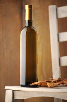 white wine bottle on a white wooden chair, with dry leaves