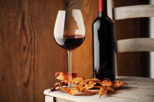  glass of red wine on a wooden chair, with dry leaves and a bottle of red wine on background