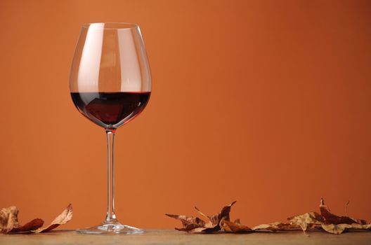 a glass of red wine in profile, on a shelf in wood, with dry leaves, on a brown background