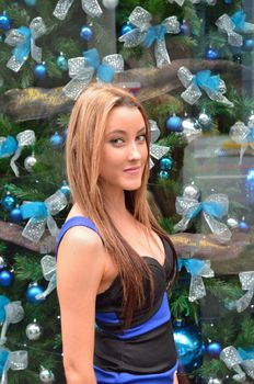 Young lady in front of a business window on Christmas Eve with a decorated Christmas tree in the background.